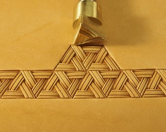 May include: A brass leather stamping tool with a triangular design is used to create a pattern on a piece of leather. The tool is being pressed into the leather, creating a series of triangles.