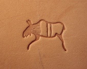May include: A close-up of a light brown leather surface with a carved image of a moose. The moose is facing left and has a detailed outline of its body and legs.