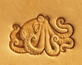 May include: A detailed carving of an octopus on a piece of light brown leather. The octopus has eight tentacles and is depicted in a curled position.