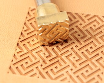 May include: A close-up of a brass leather stamping tool with a geometric pattern. The tool is being used to create a design on a piece of leather.