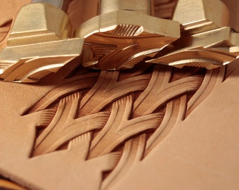 May include: Close-up of three brass leather stamping tools with a woven pattern design on a piece of leather.