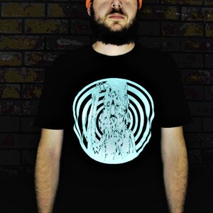 May include: A black t-shirt with a glow-in-the-dark design of a face with a spiral pattern around it.