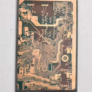 May include: Close-up of a circuit board with copper traces and green solder mask. The board has a rectangular shape and is made of a dark green material.