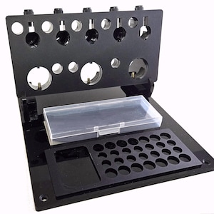 May include: A white ceramic mug with a black handle and the text "But First, Coffee" in a bold, black font. The mug is set against a blurred background, suggesting a cozy setting.