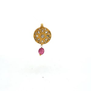 May include: A circular gold pendant featuring a central clear stone surrounded by a floral pattern of smaller clear stones. A single oval-shaped pink gemstone hangs from the bottom of the gold disc, which includes a small loop at the top for attachment.