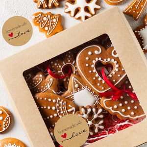 May include: A brown cardboard box with a clear window, filled with gingerbread cookies decorated with white icing and red ribbons. The box has two brown paper stickers that say "homemade with love" with a red heart.