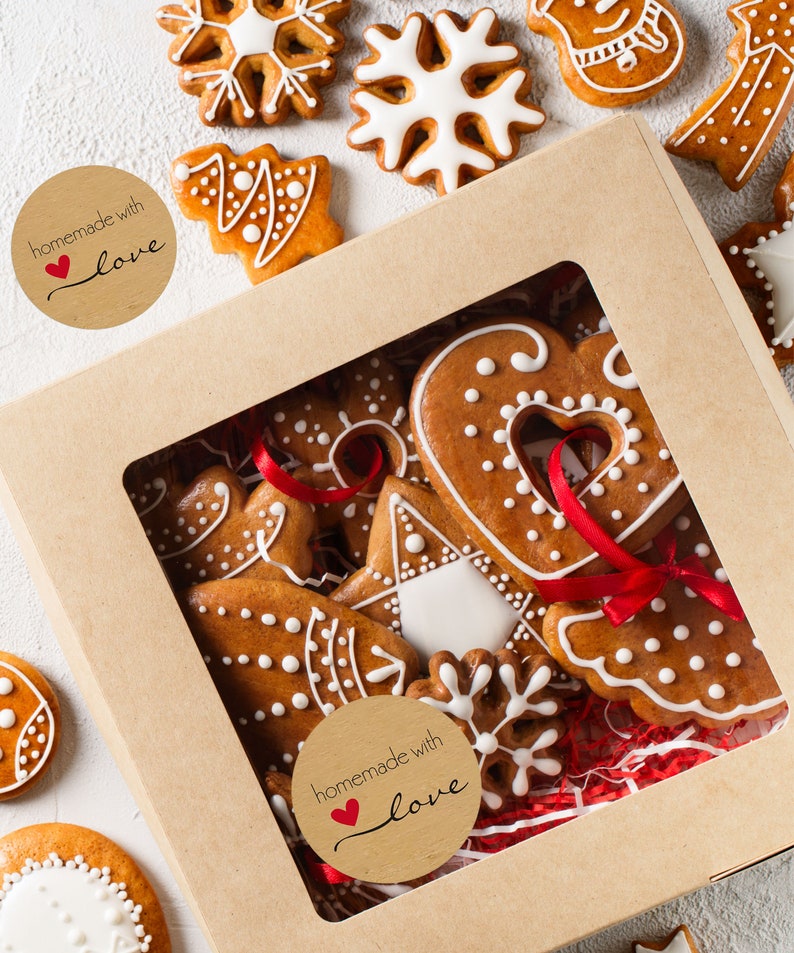May include: A brown cardboard box with a clear window, filled with gingerbread cookies decorated with white icing and red ribbons. The box has two brown paper stickers that say "homemade with love" with a red heart.