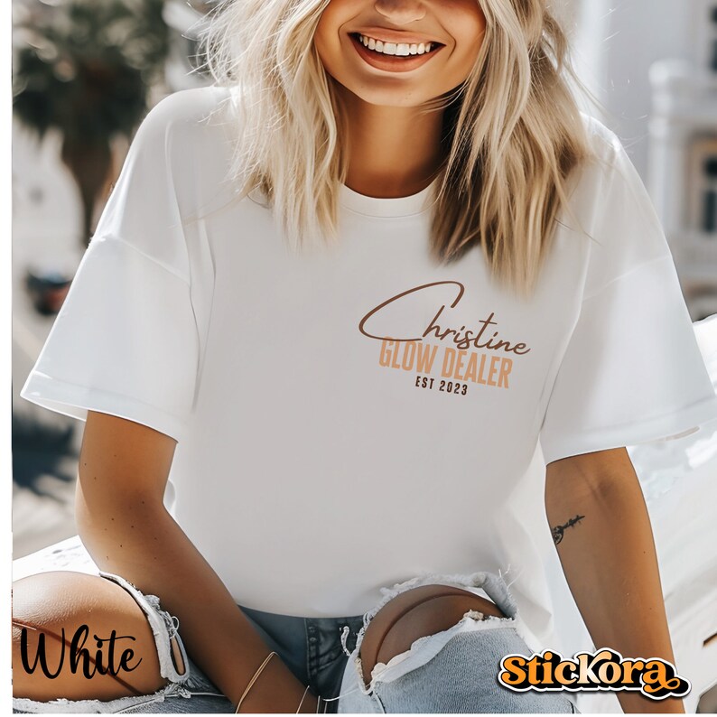 May include: White t-shirt with brown text that reads "Christine Glow Dealer Est 2023".