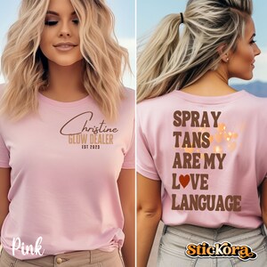 May include: Pink t-shirt with the text "Christine Glow Dealer Est 2023" on the front and "Spray Tans Are My Love Language" on the back. The shirt has a brown heart graphic on the back.