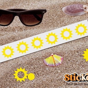 Puede incluir: Gafas de sol marrones y una concha marina sobre arena, junto a una tira de pegatinas blancas con diseños de sol amarillos. También hay una pequeña sombrilla de playa. La imagen incluye el texto "Stickora Good Times & Tan Lines."