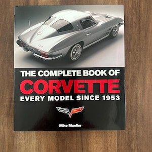 May include: A hardback book titled "The Complete Book of Corvette" with a silver Corvette sports car on the cover. The book's cover is black with red and white text, and the Corvette logo.