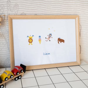 May include: A framed print with a white background featuring five cartoon characters: a monster, an ice cream cone, an astronaut, a mammoth, and a star. The name "Liam" is printed below the characters.