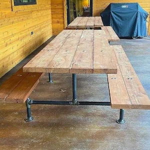 May include: A rustic wooden picnic table with black metal pipe legs. The table has two benches attached to either side. The table is made of reclaimed wood and has a natural finish.