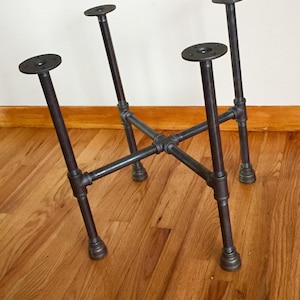 May include: A black metal table base with four legs and a square top. The base is made of industrial pipe fittings.