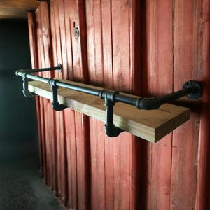 May include: A rustic wall shelf made from a light-colored wooden plank and black metal pipes. The shelf is mounted on a red wooden wall, creating an industrial and vintage aesthetic. The shelf is approximately 36 inches long.