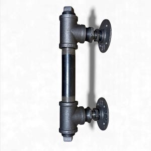 May include: A black industrial-style door handle made from metal pipes and fittings. The handle features a vertical pipe section connected to horizontal sections with circular mounting plates on each end. The hardware is painted black and has a rustic appearance.
