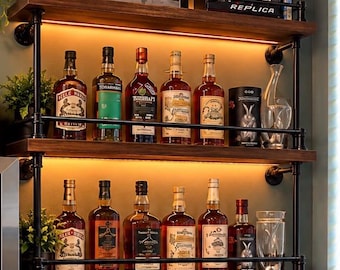 May include: A two-tier wall-mounted shelving unit made of dark wood planks and black metal industrial pipes. Each shelf features integrated warm LED lighting and a protective front rail. The shelves hold various glass liquor bottles.