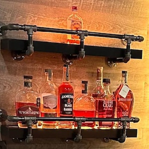 May include: Two black metal shelves with a black metal pipe railing. The shelves are filled with various bottles of liquor, including WhistlePig, Jameson Black Barrel, Elijah Craig, and Russell's Reserve. The shelves are mounted on a wood wall.