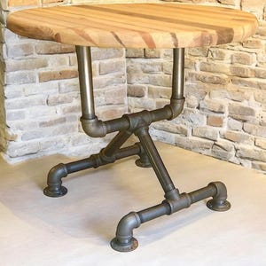 May include: A round wooden table with a light brown tabletop and a metal pipe base. The tabletop is made of wooden planks. The base is constructed from industrial-style metal pipes and fittings, creating a unique, sturdy design.