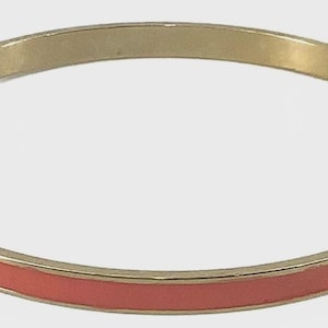May include: A gold-toned bangle bracelet with a coral-colored enamel band. The bracelet has a simple, elegant design, suitable for everyday wear. The coral band is centered within the gold frame.