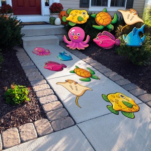 May include: A set of colorful, cartoon-style sea creatures, including a starfish, octopus, fish, turtle, and stingray, are arranged on a gray concrete walkway. The creatures are printed on a flat surface, creating a fun and whimsical outdoor scene.