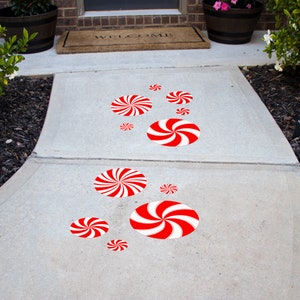 May include: A concrete walkway decorated with red and white peppermint candy cane stickers. The stickers are arranged in a path leading to a front door.
