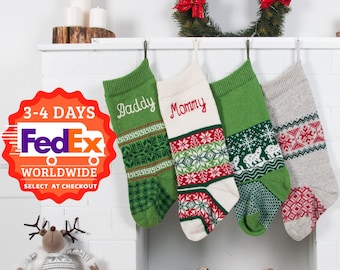 May include: Four Christmas stockings hanging on a white brick fireplace mantel. The stockings are green, red, and white with a fair isle pattern. The stockings are personalized with the names "Daddy", "Mommy", and two others. A green wreath with red bows hangs above the stockings.