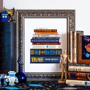 May include: A framed print of a stack of books with the title "Dune" by Frank Herbert on the bottom. The books are arranged in a bookshelf with other books and decorative items.