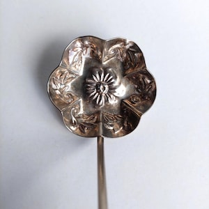 Könnte beinhalten: Ein silberfarbener Servierlöffel mit floralem Design auf der Schale. Die Schale ist wie eine Blume geformt und weist detaillierte Blatt- und Blütenmuster auf. Der Löffel hat einen langen, schlanken Stiel.