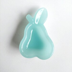 Pode incluir: Um prato em forma de pera azul claro com um acabamento brilhante. O prato tem um caule e uma base arredondada. A cor é um azul pastel suave, e o prato parece ser feito de vidro ou material semelhante.