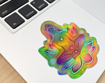 May include: A holographic sticker featuring a woman meditating in a lotus flower. The woman is surrounded by a rainbow of colors, and the sticker has a sparkly, iridescent finish.
