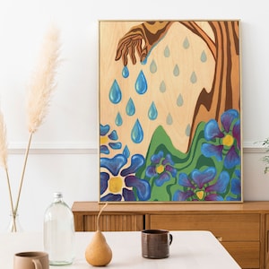 Puede incluir: Una pintura enmarcada que representa una mano que se extiende hacia abajo y libera gotas de lluvia azules sobre un campo de flores azules estilizadas con centros amarillos. El fondo es una veta de madera clara.