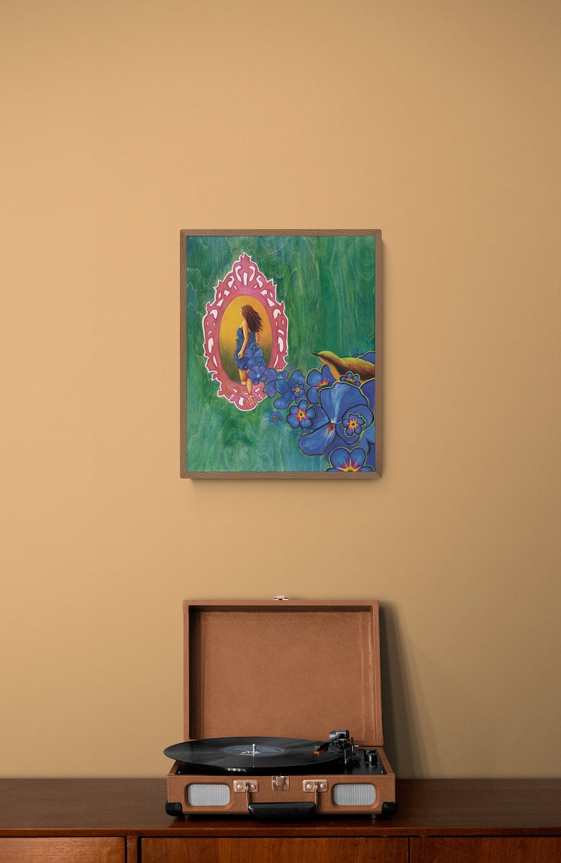 May include: A framed painting of a woman in a blue dress standing in a pink ornate frame, surrounded by blue flowers and a small bird. The painting is on a green background.