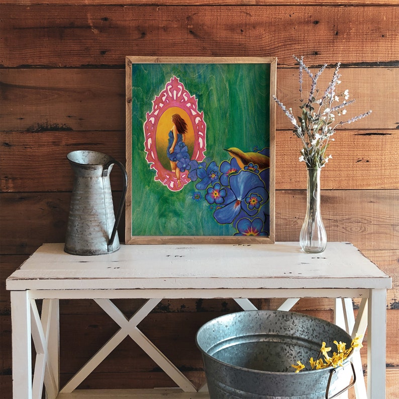 May include: A framed painting of a woman in a blue dress standing in a pink ornate frame surrounded by blue flowers. The background is a green and blue abstract design.