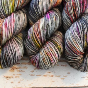 May include: Three skeins of yarn in a variegated colorway with shades of gray, black, orange, yellow, pink, and white.