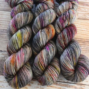 May include: Three skeins of colorful yarn in shades of grey, pink, orange, and yellow. The yarn is arranged in a circle, with the ends of the skeins overlapping.