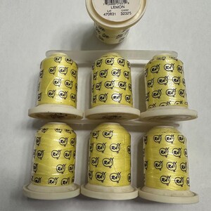 May include: A collection of yellow thread spools, labeled "LEMON", with the text "ROBISON-ANTON TEXTILE CO." and "400YD/364 M." printed on the top. Each spool is wrapped with yellow thread and features a repeating logo pattern.