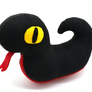 May include: Black plush snake with a yellow eye and a red tongue. The snake is curled up in a C shape.