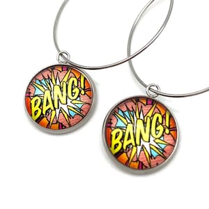 May include: A pair of silver hoop earrings with a round, colorful charm that says "Bang!" in yellow letters. The charm has a red, orange, and blue comic book style design.