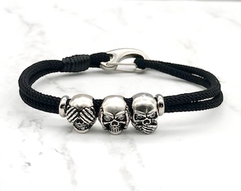 May include: Black paracord bracelet with three silver skull beads. The skulls are each depicting a different part of the "See no evil, hear no evil, speak no evil" saying.