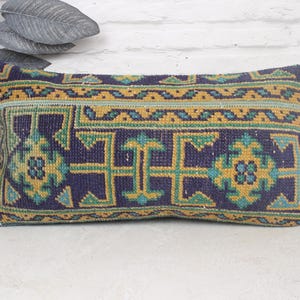 May include: A rectangular throw pillow with a blue, green, and yellow geometric pattern. The pillow is made of woven fabric and has a fringed edge.