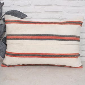 May include: A white pillow with red and grey stripes. The pillow is made of a soft, woven fabric and has a rectangular shape.