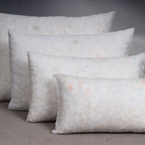 May include: Four white rectangular pillows of varying sizes are arranged in a row. The pillows are filled with a fluffy, white material, and the fabric has a slightly textured appearance. The pillows are suitable for home decor and bedding.