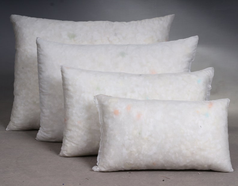 May include: Four white rectangular pillows of varying sizes are arranged in a row. The pillows are filled with a fluffy, white material, and the fabric has a slightly textured appearance. The pillows are suitable for home decor and bedding.