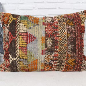 May include: Rectangular decorative pillow with a patchwork design. The pillow features a mix of colors including brown, red, yellow, and green. The design includes geometric patterns and a textured appearance, suitable for home decor.