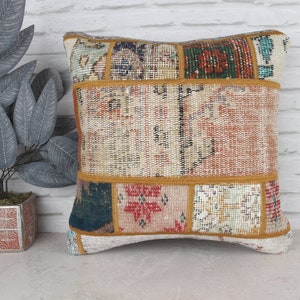 May include: A square patchwork pillow with a variety of colors and patterns, including red, orange, yellow, green, blue, and white. The pillow has a gold trim around the edges.