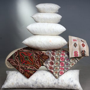 May include: A stack of white, fluffy pillows of varying sizes, with several decorative square pillows featuring colorful geometric patterns. The pillows are arranged on a curved, off-white surface, creating a layered display.