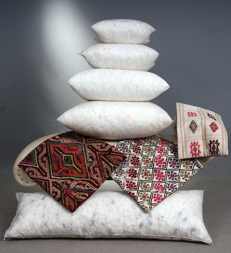 May include: A stack of white, fluffy pillows of varying sizes, with several decorative square pillows featuring colorful geometric patterns. The pillows are arranged on a curved, off-white surface, creating a layered display.