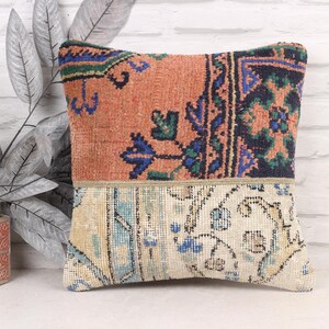 Puede incluir: Cojín decorativo cuadrado con diseño patchwork. La mitad superior presenta un fondo melocotón con motivos florales azules y verdes. La mitad inferior tiene un fondo crema con motivos florales azules.