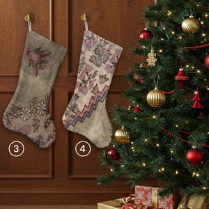 Pu&ograve; includere: Due calze di Natale con motivi floreali e geometrici sono appese a una porta di legno. Le calze sono nei toni del beige, rosa e grigio. Sullo sfondo, un albero di Natale decorato con ornamenti e regali confezionati.